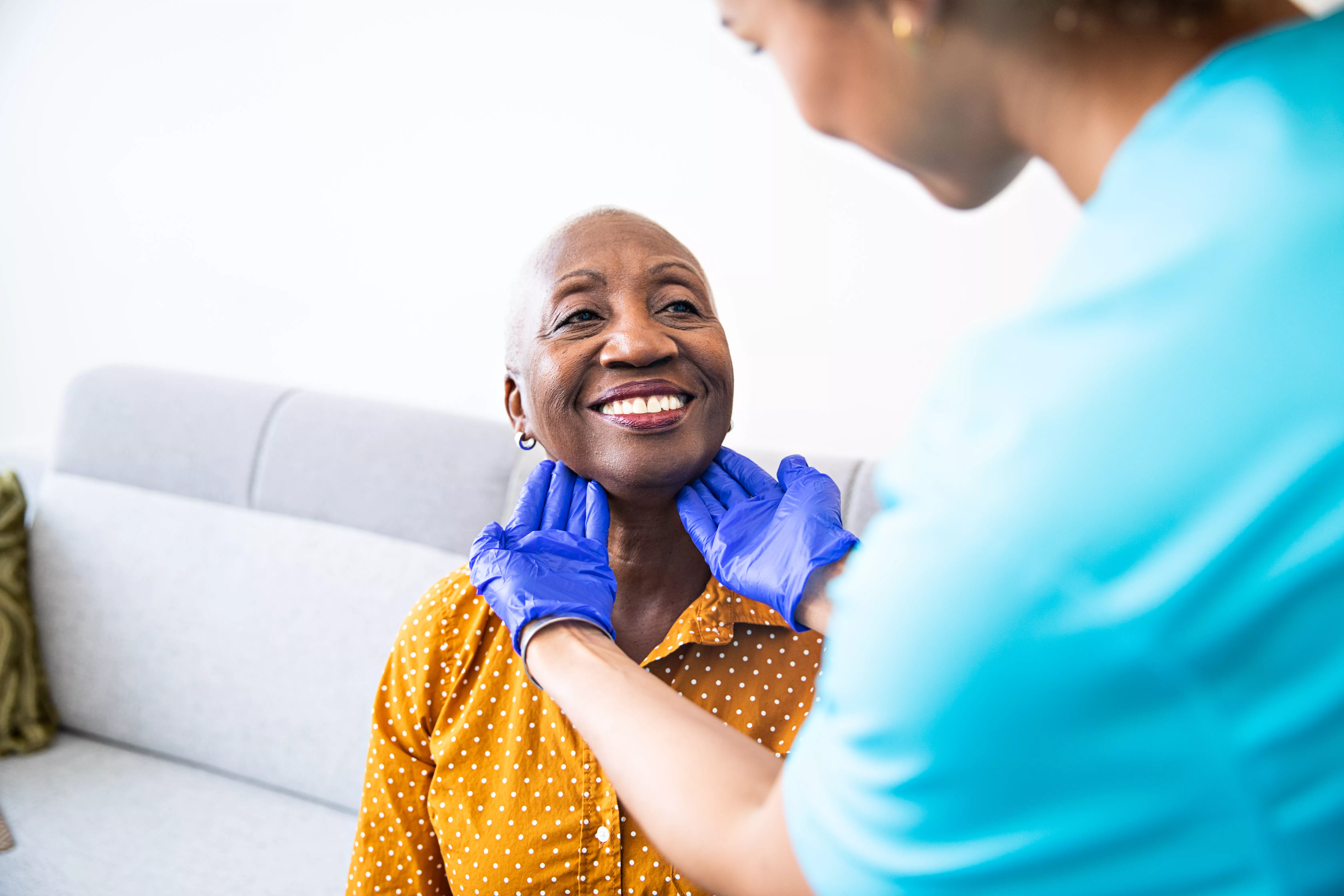 médica com as mãos com luvas azuis segurando no rosto de uma mulher negra careca sorrindo 