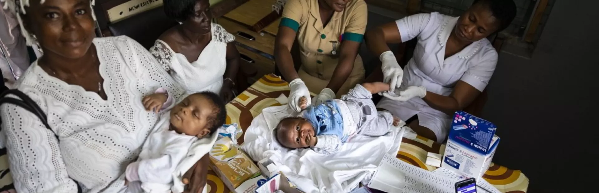 A mother holding baby in a clinic, surrounded by nurses