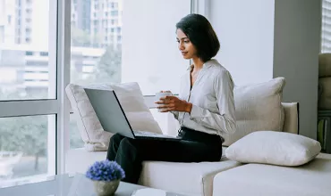 A business woman，seated on a sofa，using a laptop and holding a cup