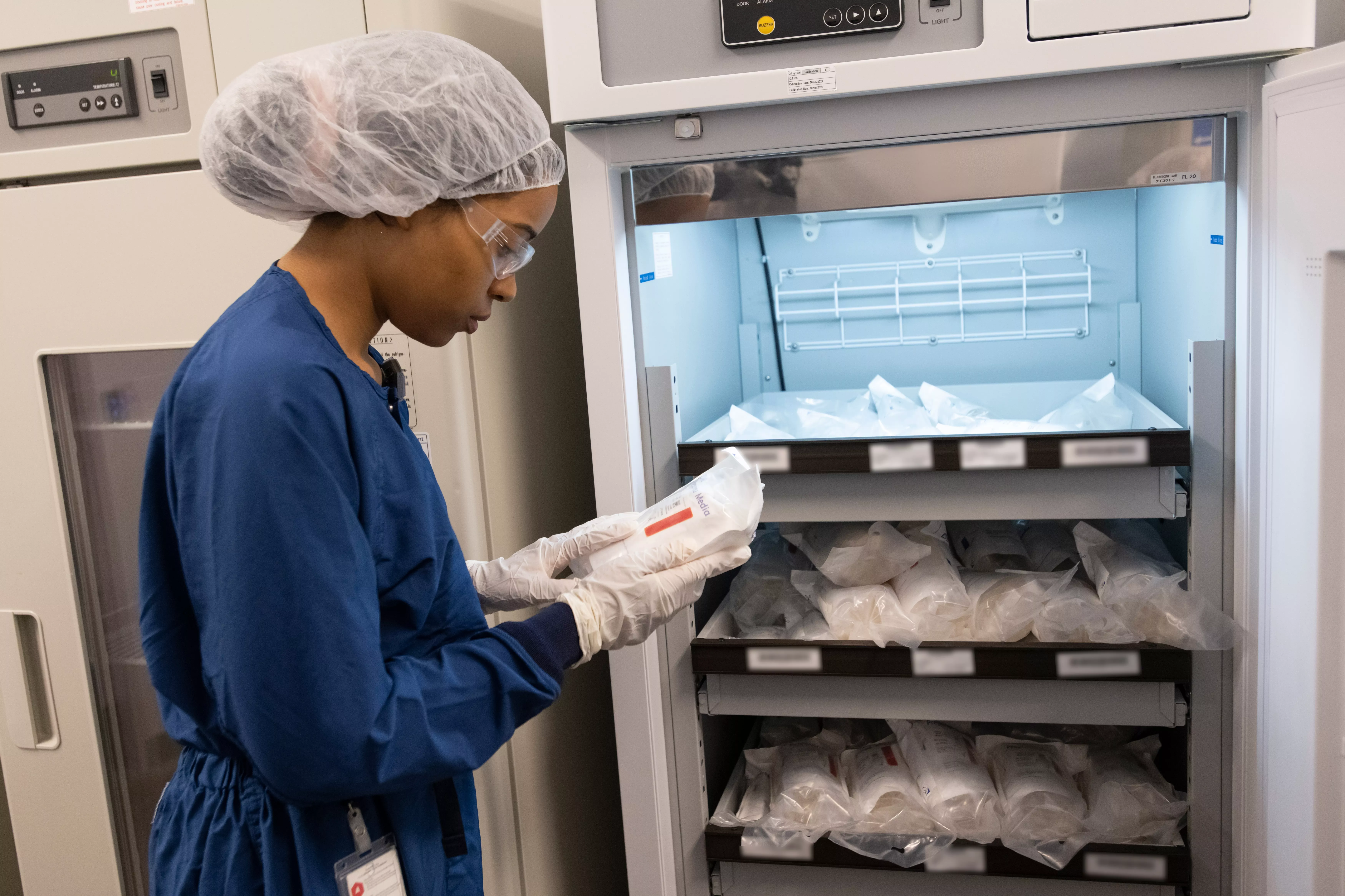 An associate in personal protective equipment stands at a refrigerator examining a bag