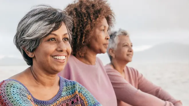 Three women sitting on a beach, looking out at the ocean. Three women sitting on a beach, looking out at the ocean.